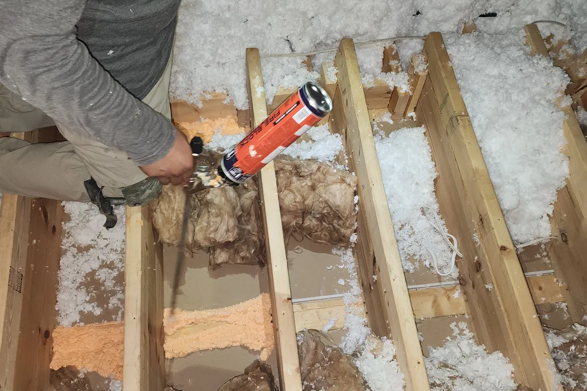 Peak Energy technician air sealing between attic joists with spray foam before insulation in a NC home
