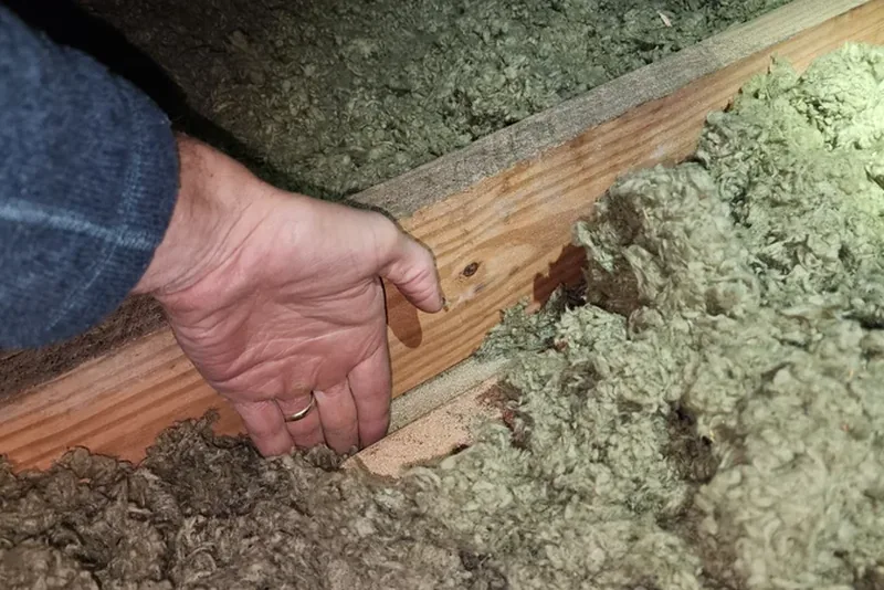 Auditor checking attic insulation depth during home energy audit in Wake County NC