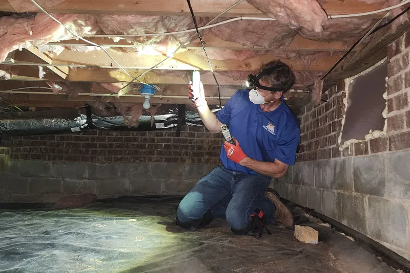 Peak Energy technician in a respirator assessing a vented crawl space with a flashlight, inspecting framing, insulation, and moisture conditions in a Wake County NC home
