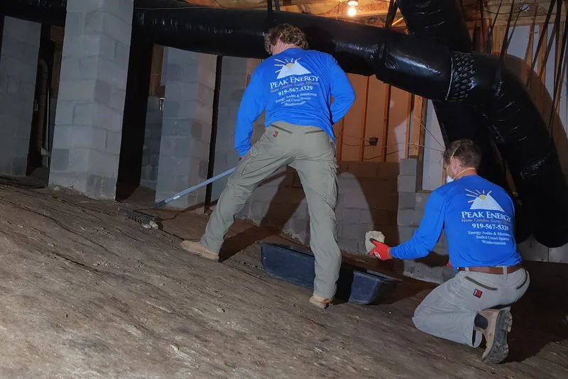 Peak Energy crew scraping old debris off the dirt floor of a Wake County crawl space before liner installation