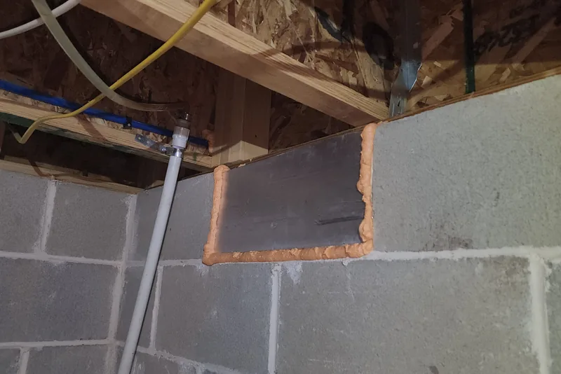 Foundation vent permanently sealed with a foil-faced rigid foam board panel and spray foam around the edges in a block-wall crawl space in NC