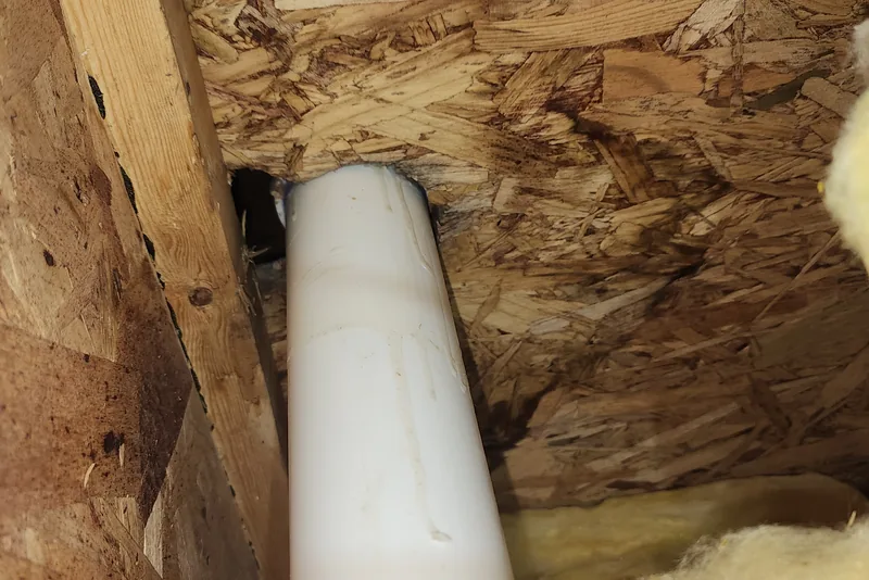 Pipe penetration left unsealed through bare subfloor with exposed fiberglass insulation in a crawl space in NC