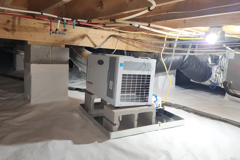 Crawl space dehumidifier mounted on a cinder block stand in an encapsulated Wake County NC crawl space, with white vapor barrier on the ground and insulated ductwork overhead