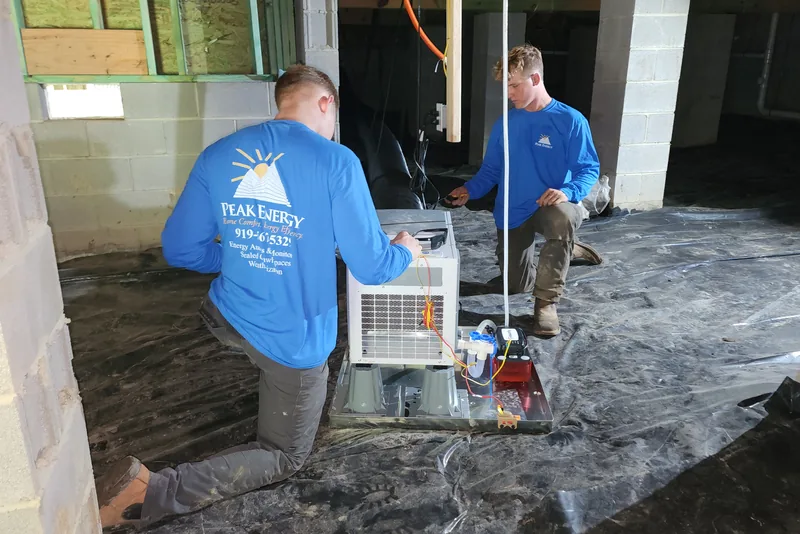Two Peak Energy technicians servicing a crawl space dehumidifier system in a Wake County NC home