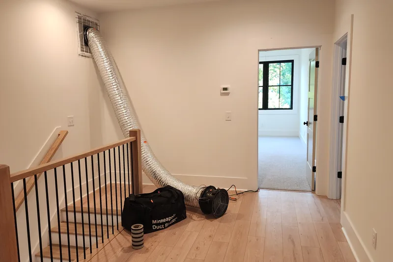 Minneapolis Duct Blaster fan and flex duct connected to a ceiling return grille in a finished new construction home in Wake County NC, set up in the stairway hall for a final duct leakage test before closing