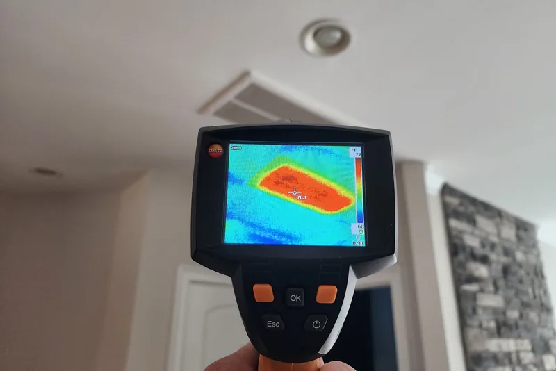 Peak Energy technician holding a Testo thermal imaging camera showing heat loss around a ceiling register in a Triangle NC home