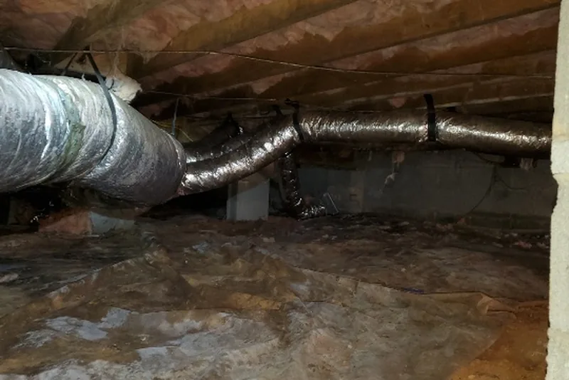 Vented crawl space with exposed HVAC ductwork and a damp vapor barrier on the ground in a Triangle NC home