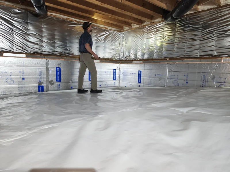 Peak Energy technician inspecting a completed crawl space encapsulation in a Triangle NC home — sealed walls and white vapor barrier