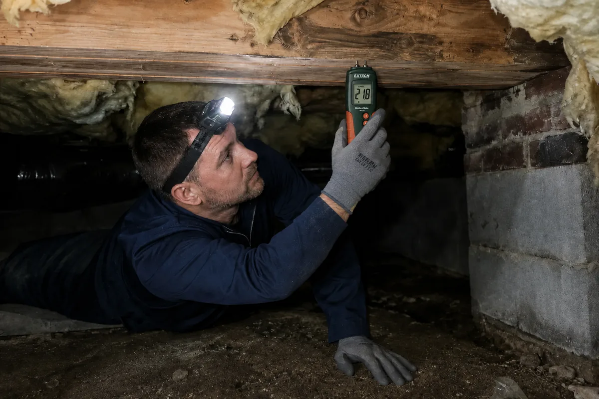 Peak Energy technician taking a wood-moisture reading on a floor joist during a crawl space inspection in Wake County NC