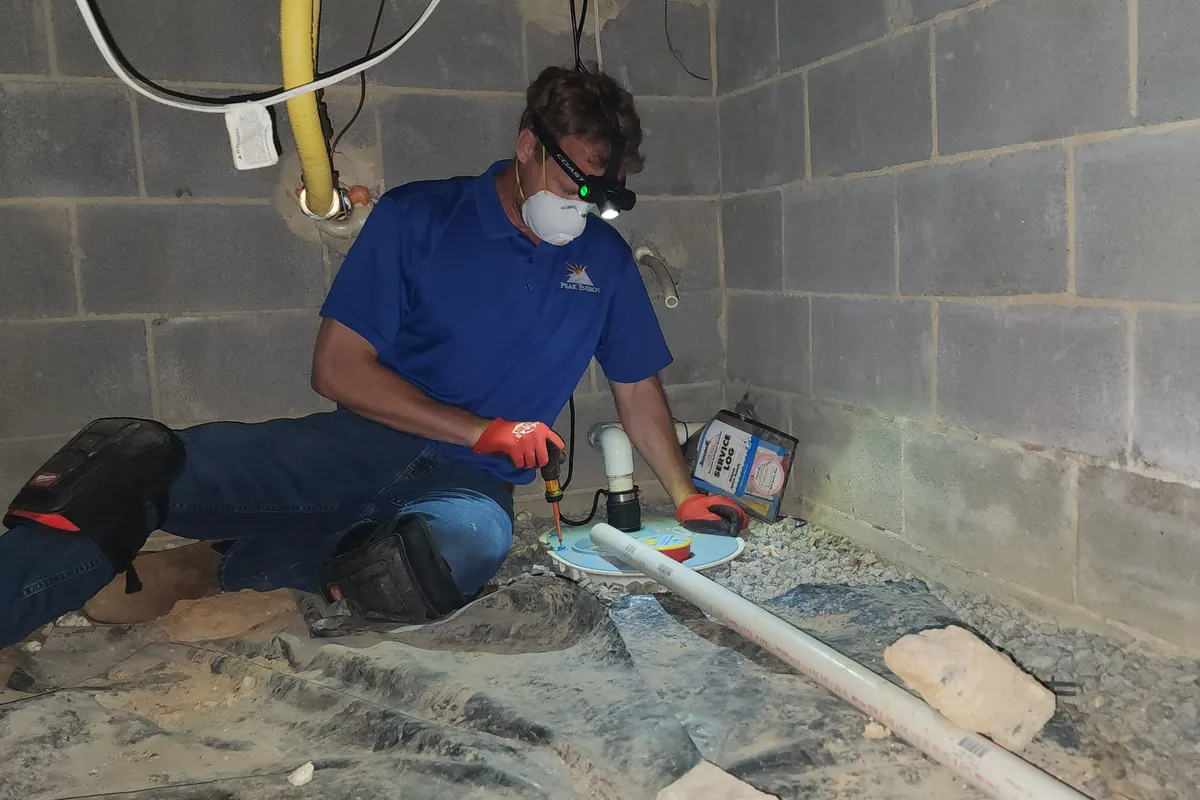 Peak Energy technician checking a crawl space sump pump and discharge line during an inspection in the Triangle NC