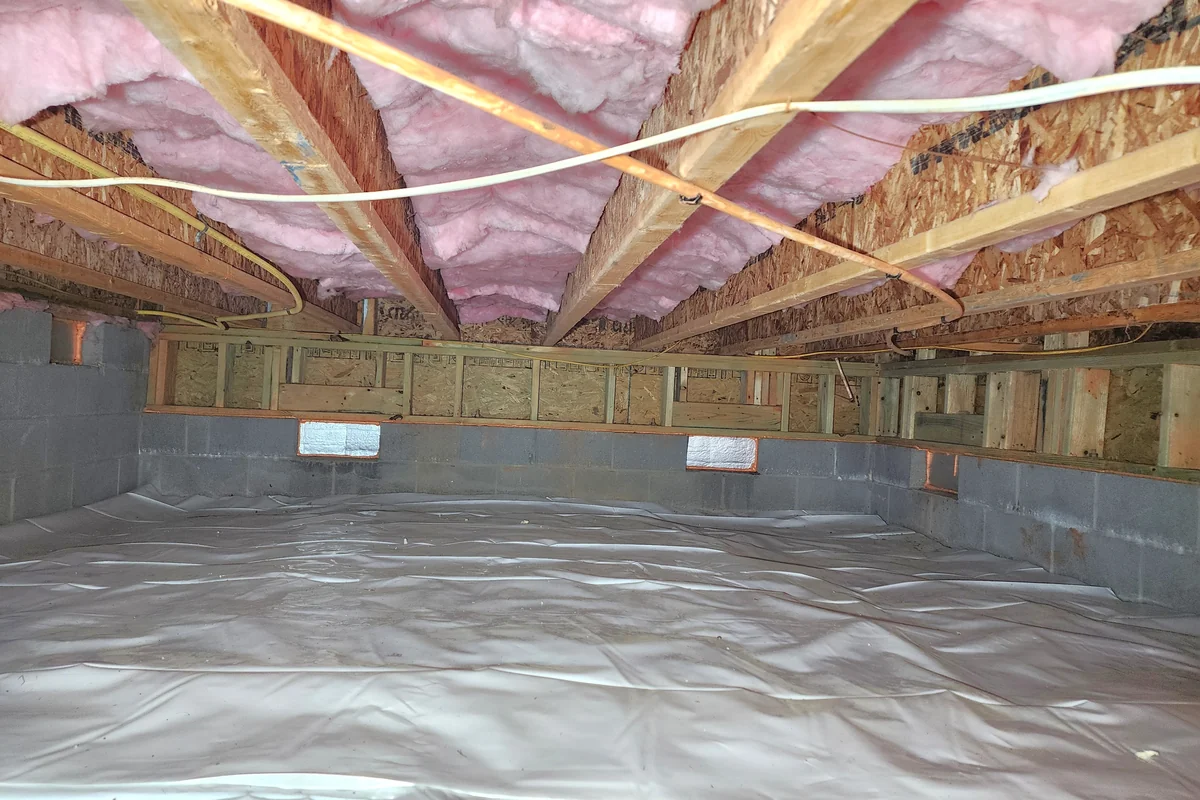 Vented crawl space with vapor barrier on the floor and pink fiberglass batt insulation between the joists overhead, foundation vents still open