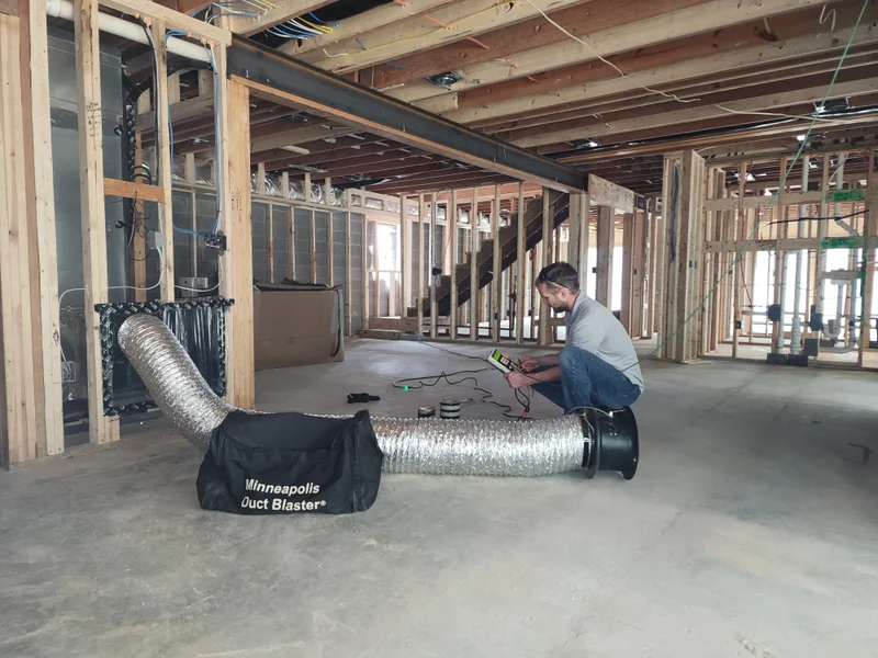 Technician performing duct leakage test with duct blaster fan in new construction