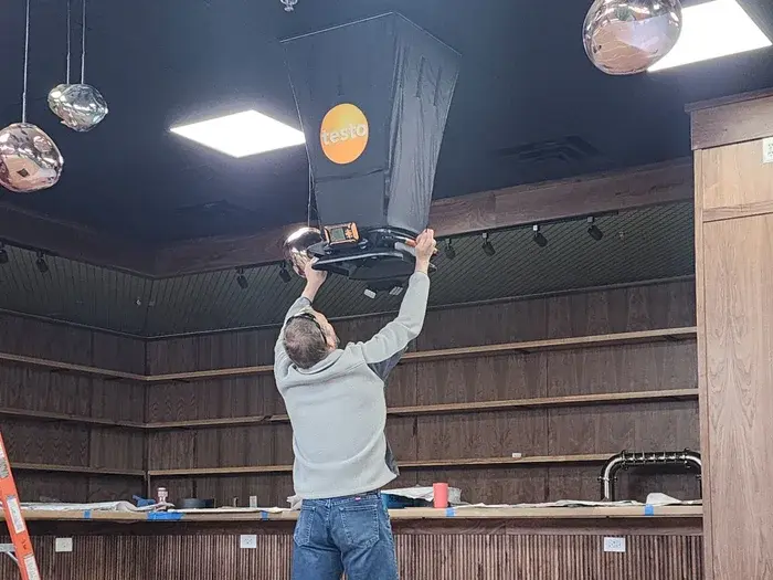 Technician measuring airflow with flow hood on ceiling register in NC building