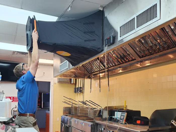 Technician testing commercial kitchen exhaust hood airflow with flow hood in NC