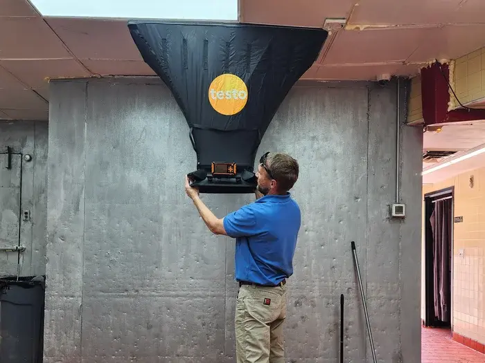Technician using flow hood on wall register to measure HVAC supply airflow in NC